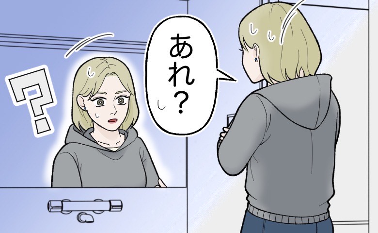 上パーカー・下ジーンズ姿の女性が、鏡の前に立って違和感を感じている様子
