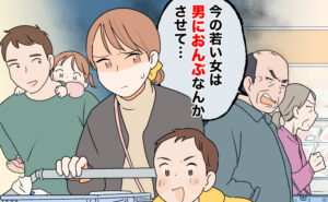 家族でスーパーの買い物中、通りがかりの年配男性から、下の子をおんぶする夫に対し「今の若い女は男におんぶなんかさせて…」と嫌みを言われ、暗い表情になる女性。年配男性の隣には妻らしき女性がおり、怪訝そうな顔で男性を見ている。